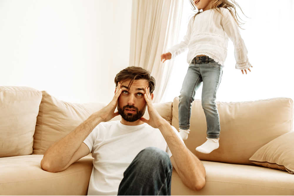 Rambunctious child jumps on a couch while exasperated dad come to his wit's end