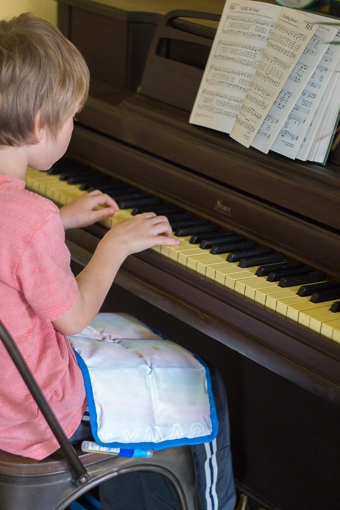 A young boy playing the piano with a weighted lap pad on his lap. 