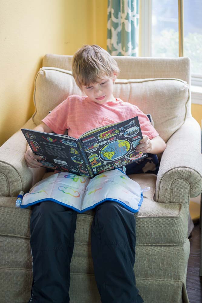 A child reading a book while having the weighted lap pad resting on him. 