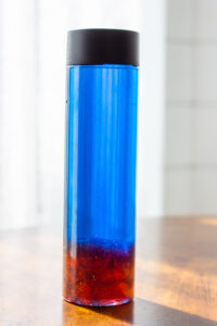 Close up of a glitter glue sensory bottle. Blue on top, red glitter glue on bottom. 