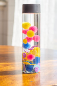 Close up of a sensory bottle with buttons and pompoms inside. 