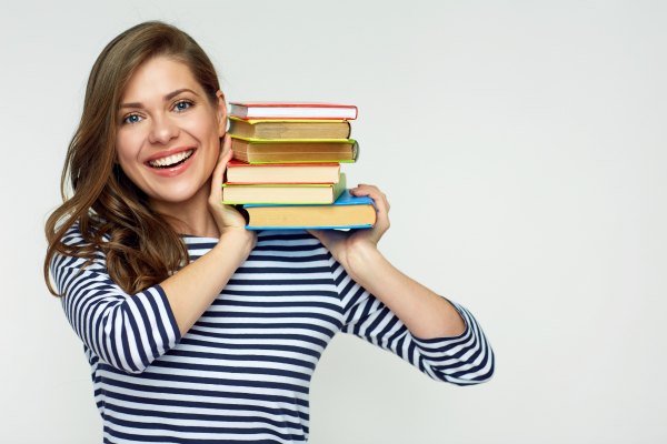 Image of a mom holding a stack of books on her shoulder and smiling. 
