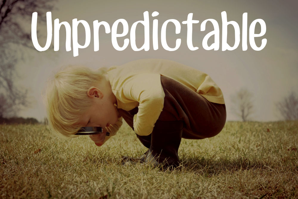 A young child is bending down looking in the grass, investigating something with a magnifying glass.  Vintage style color.