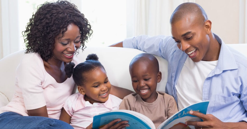 Black family of four sitting on a couch reading aloud.