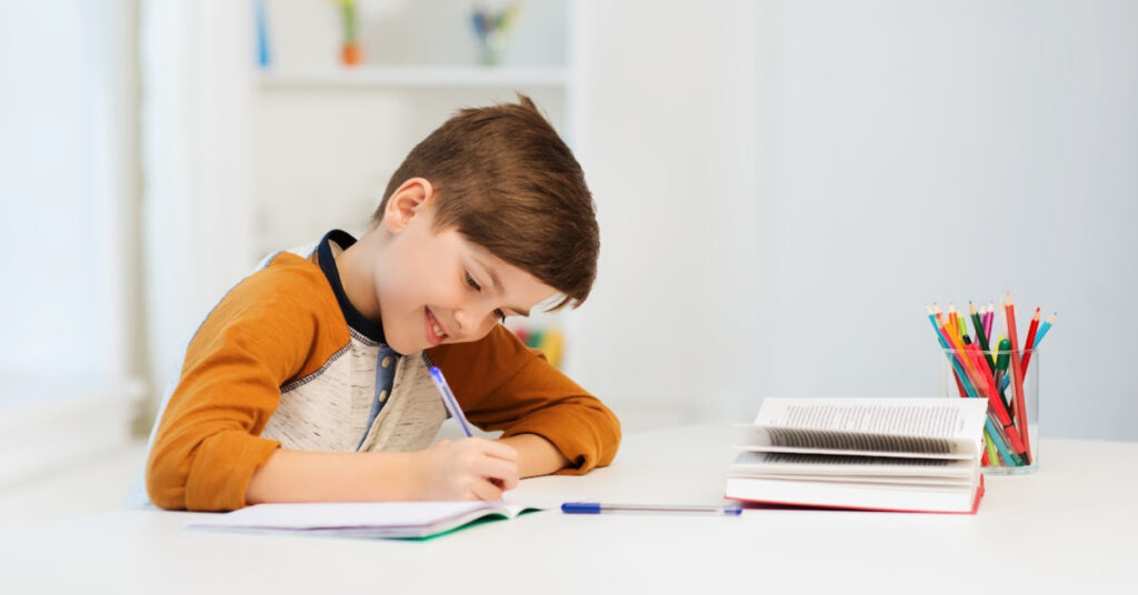 A white boy at a desk writing in a notebook.